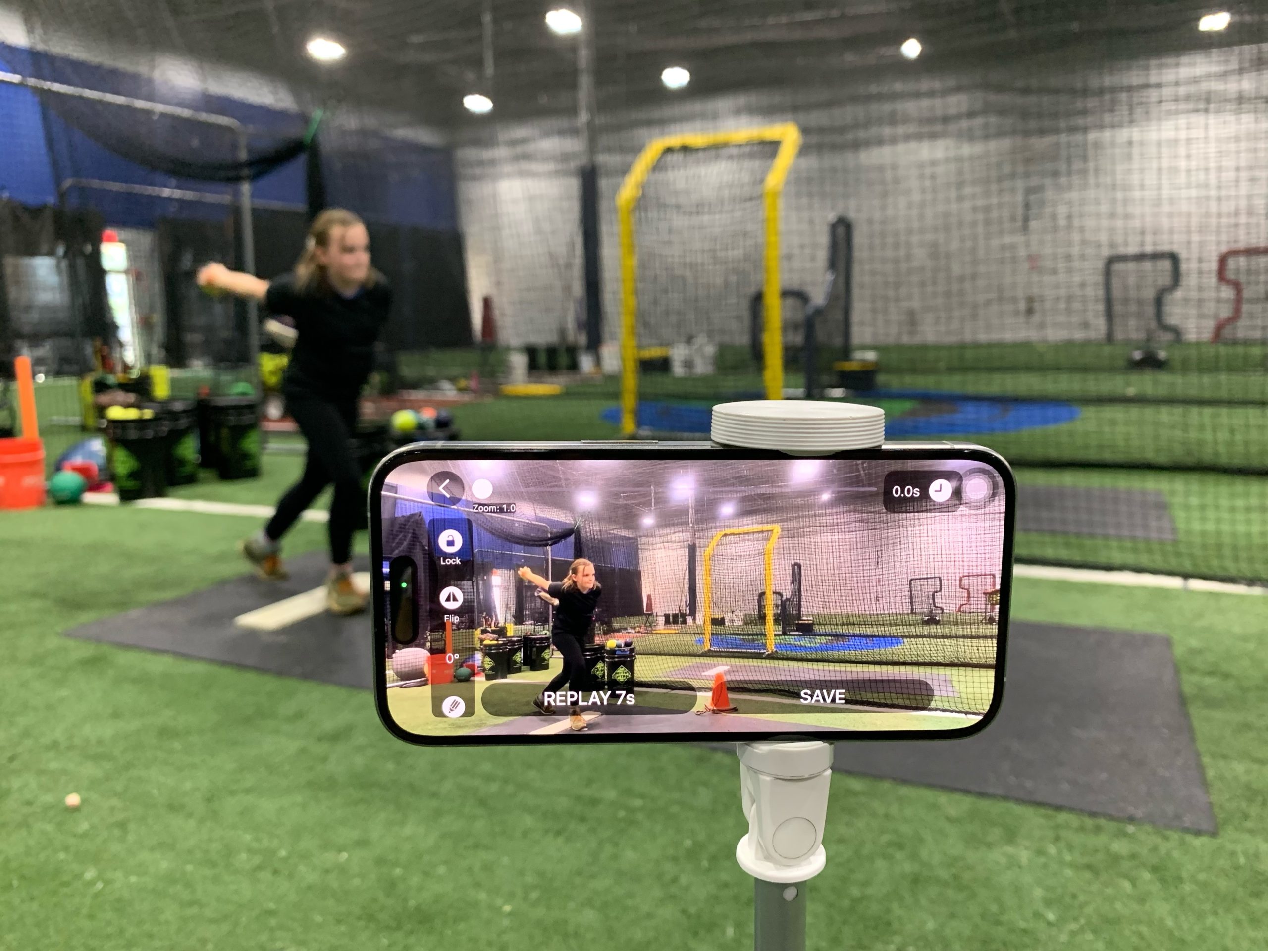 softball pitching cage training session: Video Delay instant Replay app in front of a young pitcher girl throwing a ball.